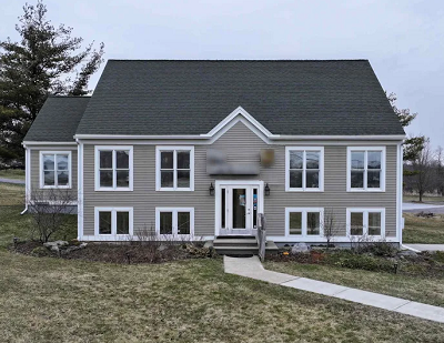 Three-story cape-style house with munton windows and taupe clapboard siding.