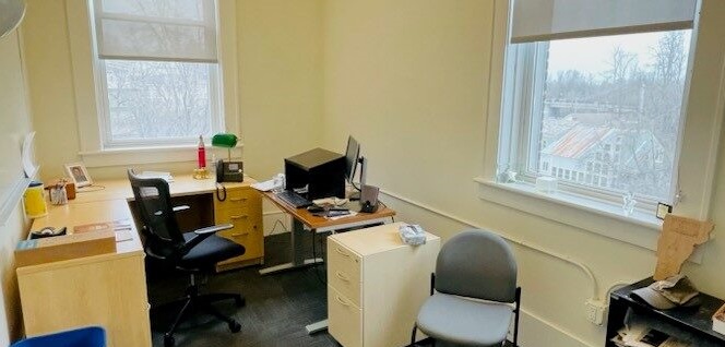 View of office, with desk, whiteboard, computer, and bookshelves with lots of light from windows. 