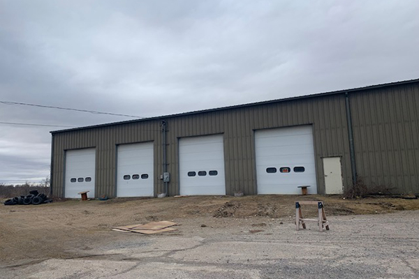 Large beige warehouse with 4 white overhead doors on paved lot.