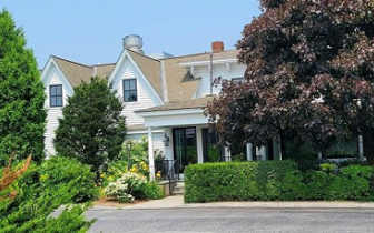 Exterior of Two-story white clapboard New England Inn behind artfully landscaped front foliage.